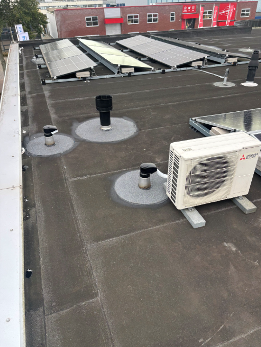 Airco buitenunit op plat bitumen bedrijfsdak met zonnepanelen