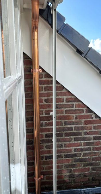 Nieuw geplaatste koperen regenpijp langs gevel